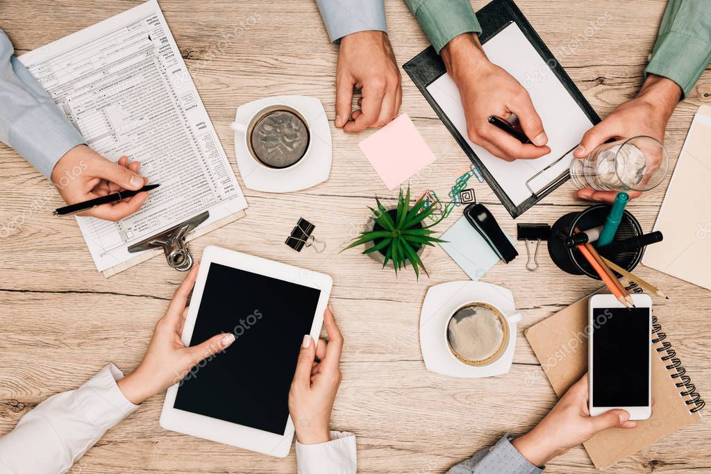 Top view of colleagues working with gadgets and documents with coffee on table, cropped view