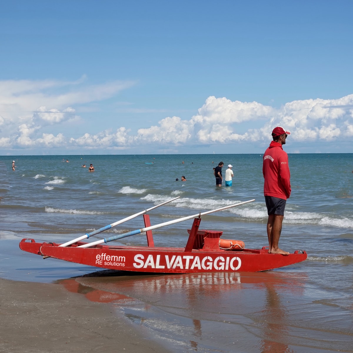 man in white t-shirt and blue shorts standing on red and white kayak on sea