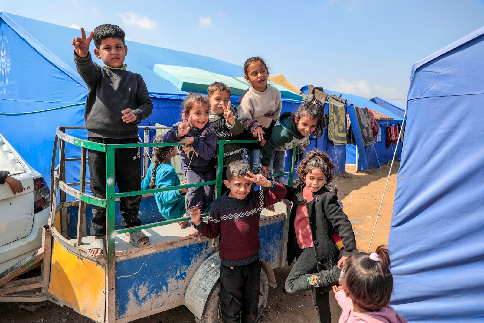 Smiling children pose in front of tents at a refugee camp.