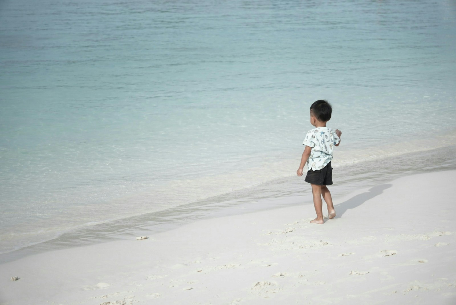 a young boy standing on top of a sandy beach