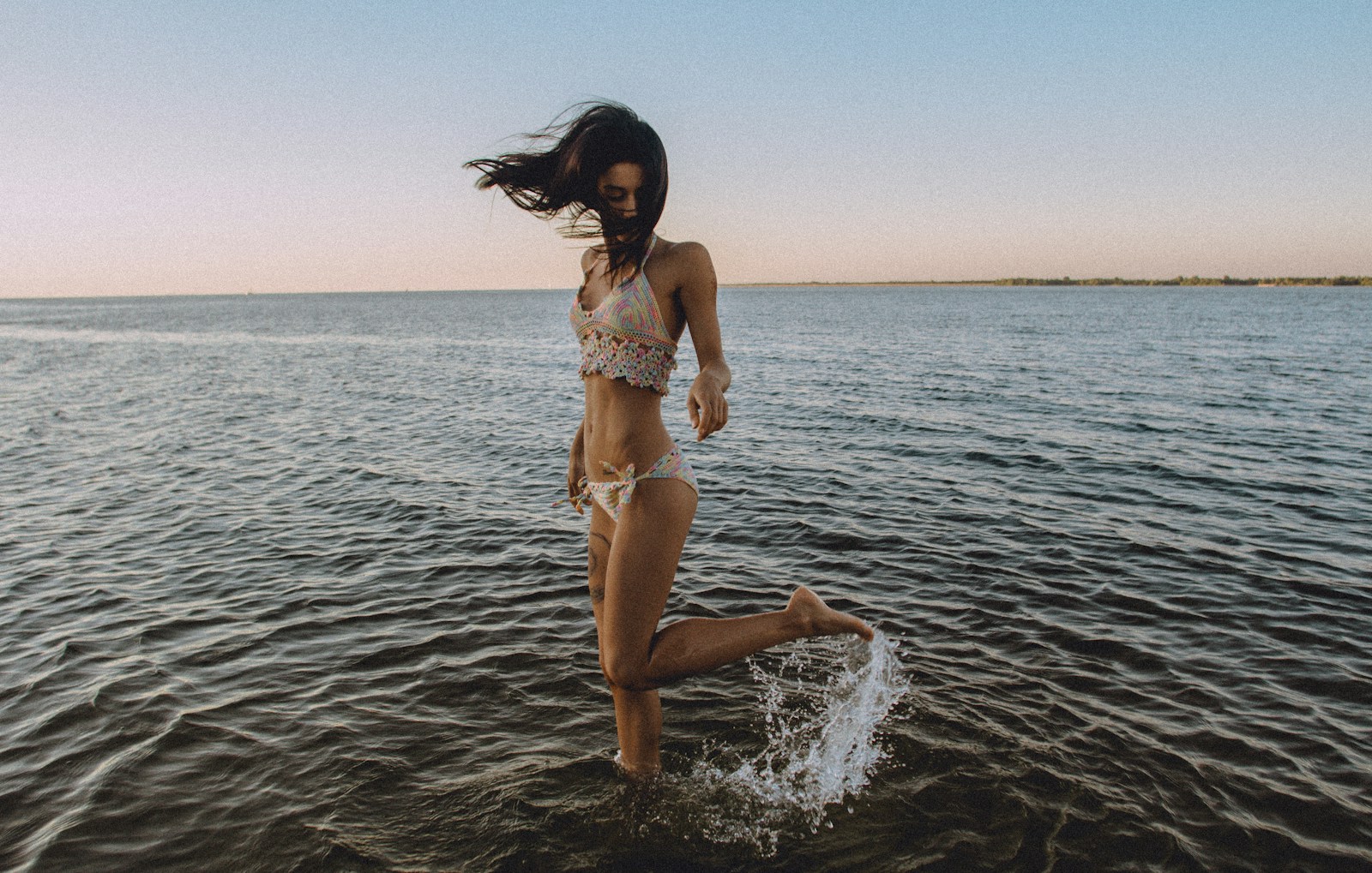 A girl in a bikini flicks her leg up behind her in the water at a beach