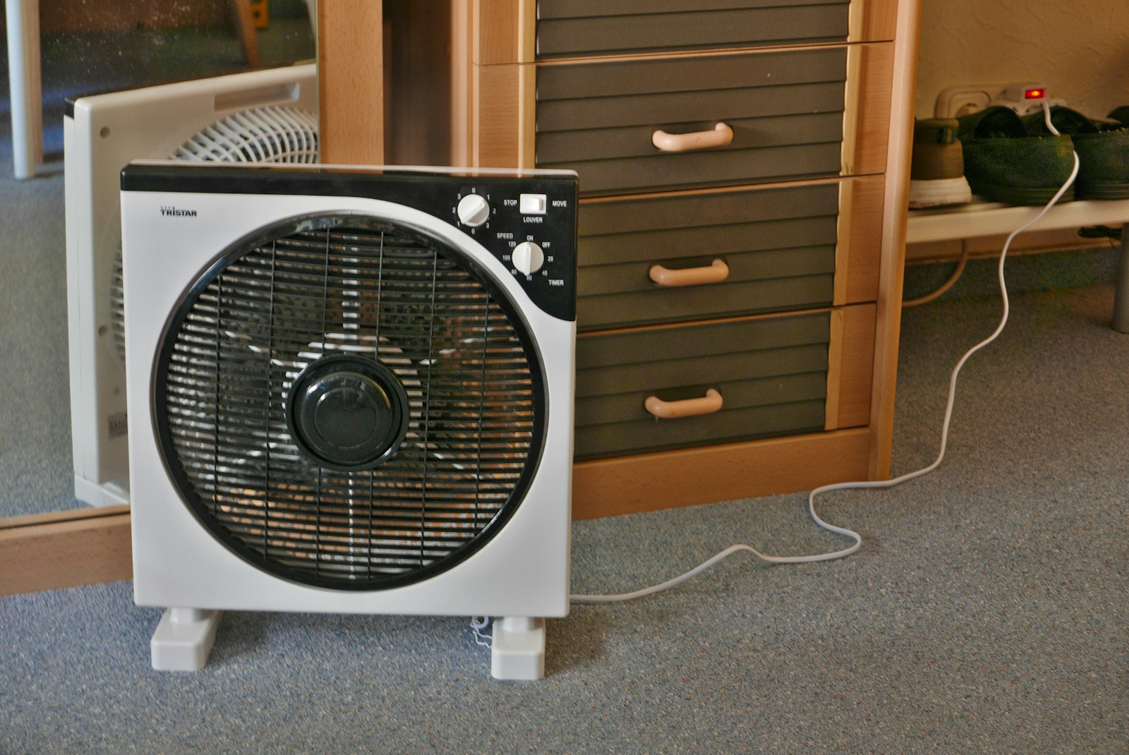 A fan is positioned near a dresser and mirror.