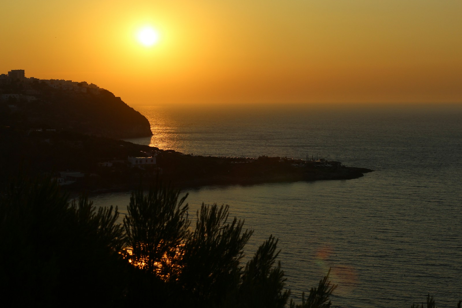 Sunset over a calm ocean with coastal hills