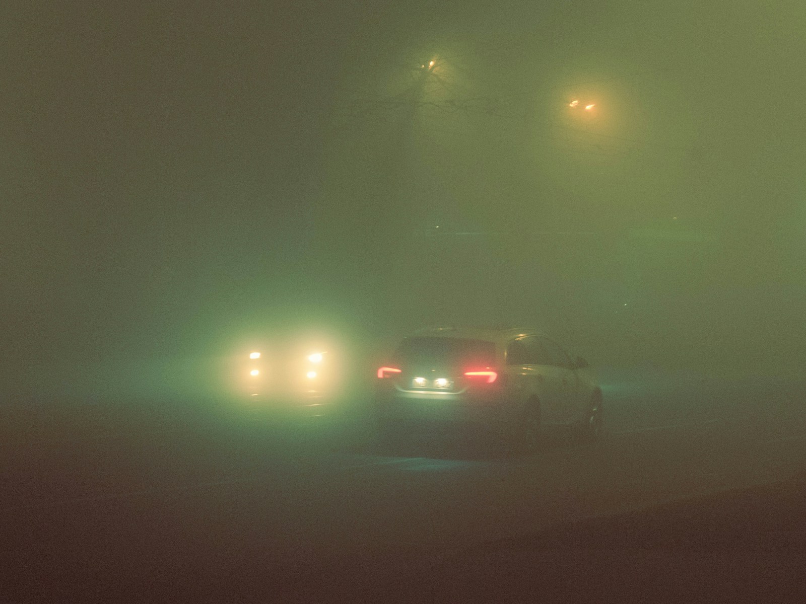 Cars drive on a foggy road at night.