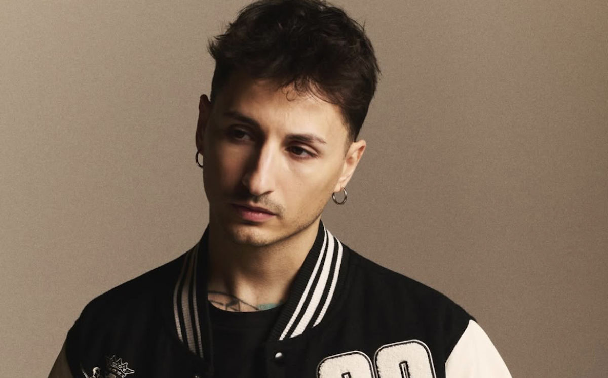 Nayt in primo piano con giacca varsity nera e orecchini, ritratto del rapper in gara a Sanremo 2026.