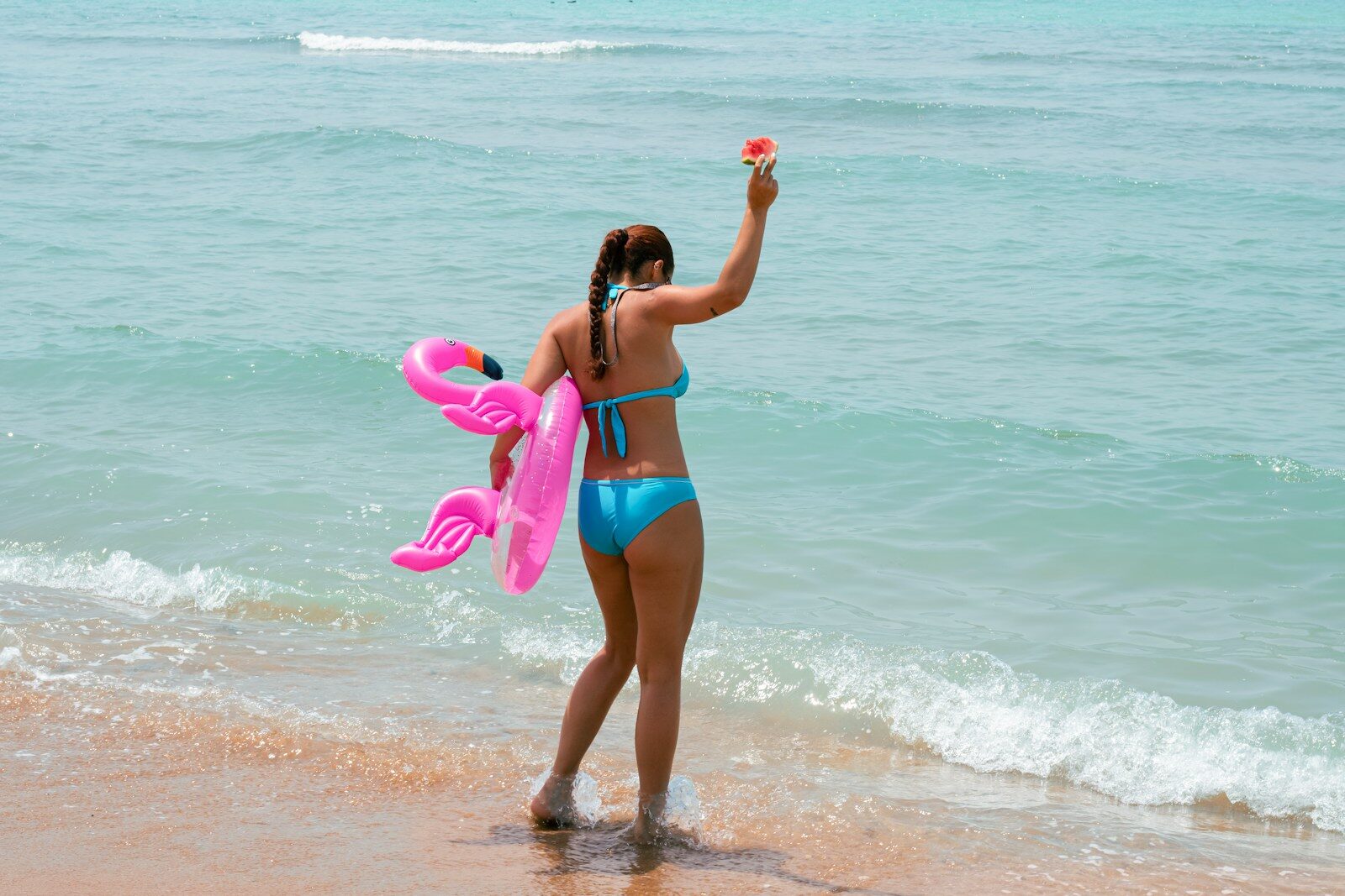 Woman with pink inflatable waving on beach