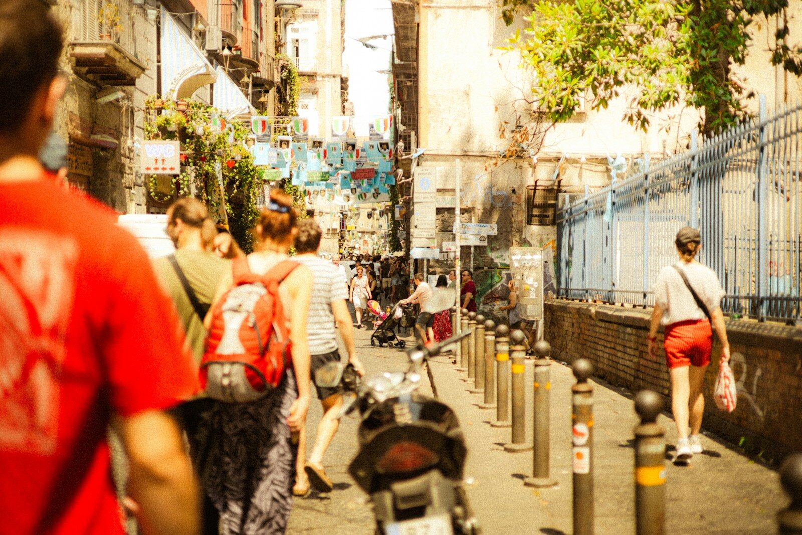 People walk down a sunlit street in a city.