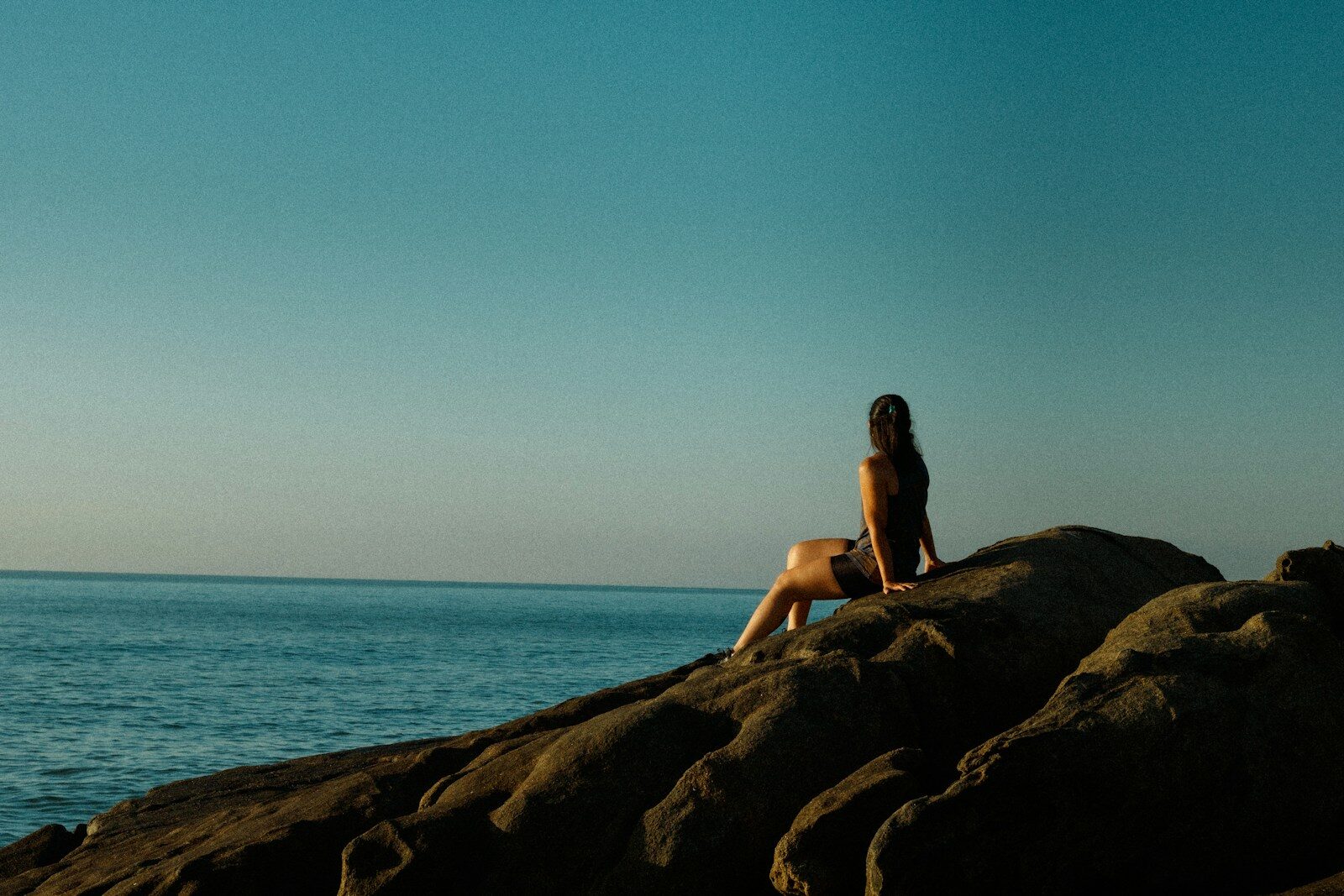 a woman sitting on top of a rock next to the ocean